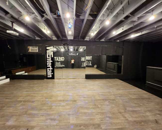 An empty dance studio with wooden flooring, mirrored walls, and overhead lights.