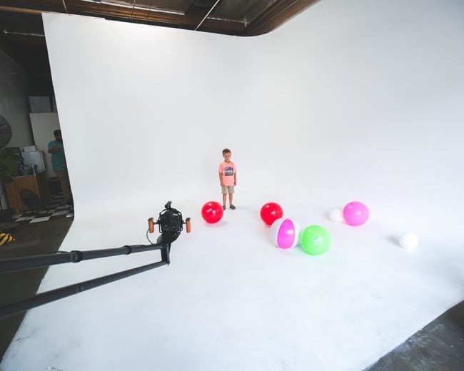 A child stands on a white background surrounded by colorful balls of various sizes.