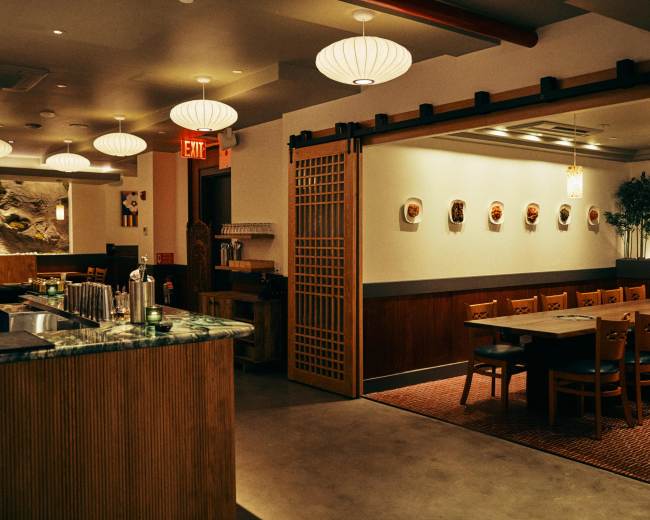 The image shows a modern restaurant interior with wooden accents, a bar area, and a dining space featuring hanging paper lanterns and framed artwork on the walls.