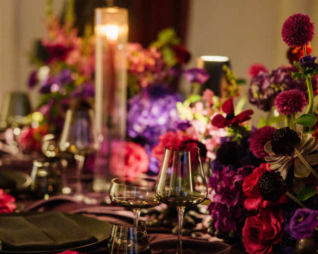 A richly decorated dining table is adorned with vibrant floral arrangements, glassware, and elegant table settings.