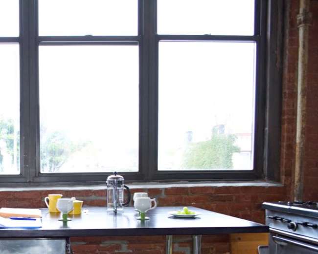 A simple dining table is set near large windows with a view of an urban landscape.