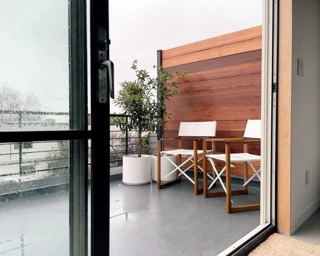 A balcony features two white chairs and a potted plant against a wooden wall.