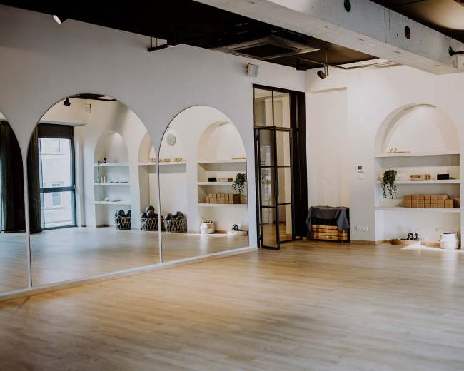 The image shows a spacious, well-lit studio with arched wall niches displaying neatly arranged fitness equipment and decor.