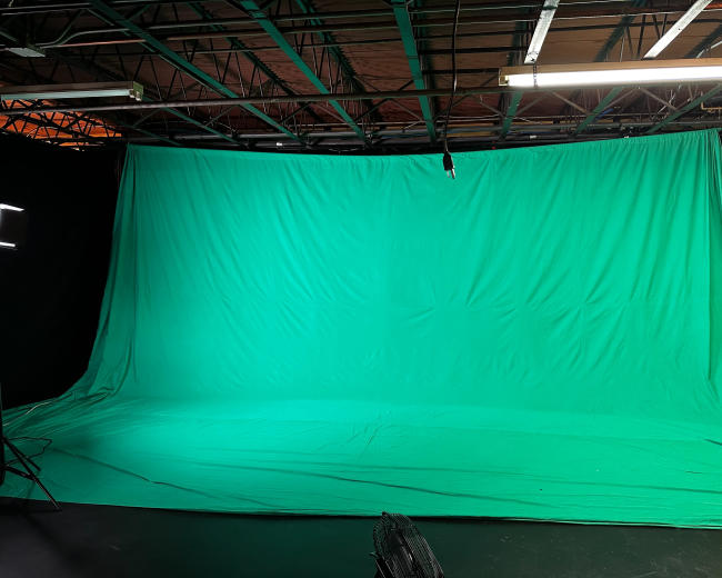A large green backdrop set up in a studio space with visible lighting equipment and studio infrastructure.