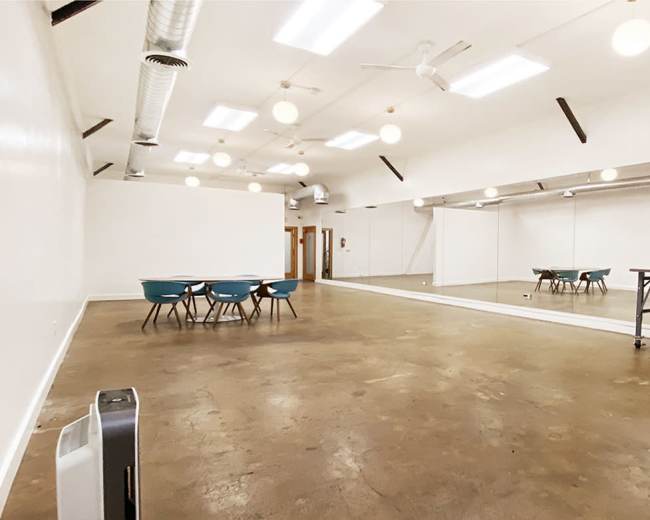 The image shows a spacious, empty room with a polished concrete floor, a mirrored wall, and several tables and chairs arranged in the center.