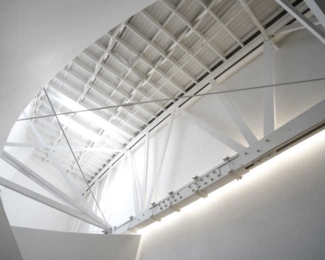 The image shows a modern interior space with a curved ceiling supported by metal beams and bright overhead lighting.