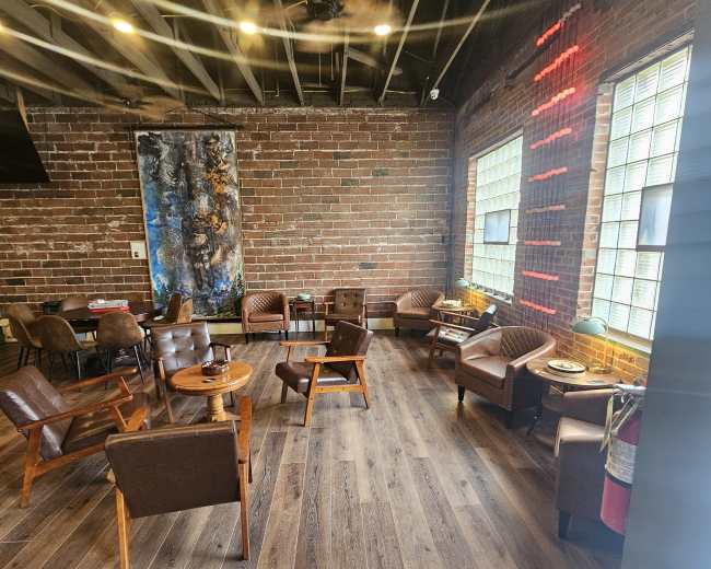 The image depicts a cozy café interior featuring wooden flooring, brick walls, and various seating arrangements, including leather chairs and tables.
