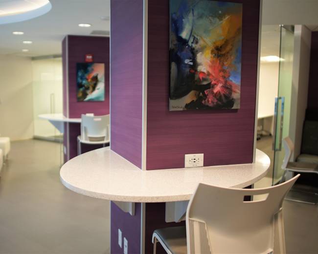 The image shows a modern, minimalist interior space with purple walls, circular tables, and contemporary art on display.