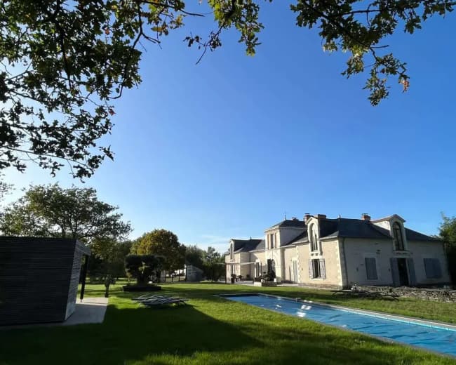 A modern house with a blue pool and green lawn is set against a clear blue sky.