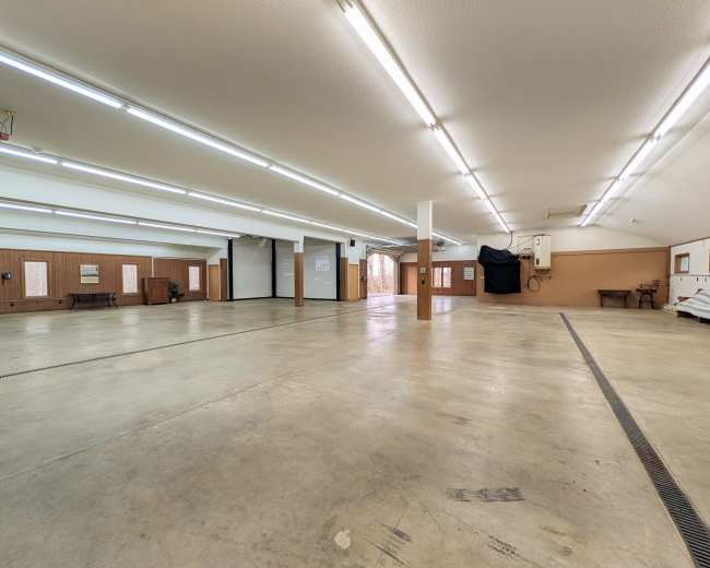 The image shows a spacious, well-lit interior area with concrete flooring and wooden paneling, featuring multiple entry points and a large, open floor plan.