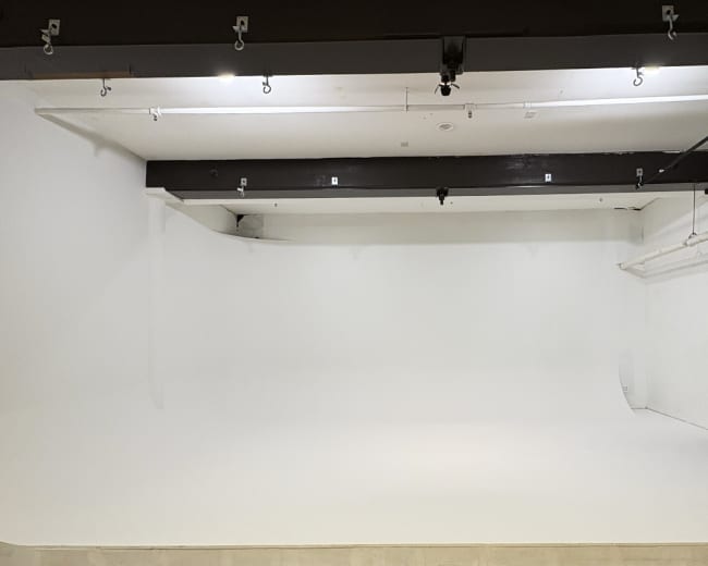 The image shows a spacious interior photography studio with a seamless white backdrop and soft lighting.