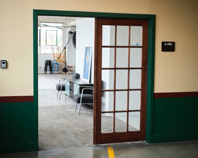 A wooden-framed glass door leads into a bright, open office space featuring minimalist furniture.