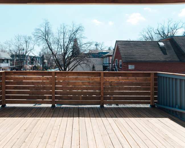 A wooden deck overlooks a neighborhood with houses and bare trees under a clear sky.
