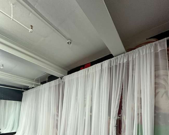 The image shows a room divided by sheer white curtains, creating separate spaces within the area.