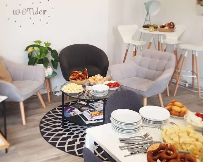 A cozy gathering space features gray armchairs and a white dining table adorned with plates of sliced cheese, fruit, and pretzels.