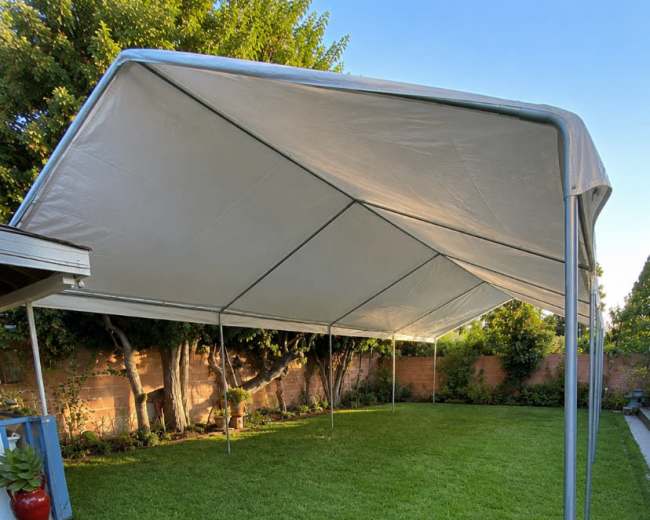 A large white canopy tent is set up on a green lawn surrounded by trees and bushes.