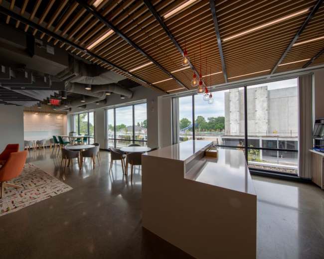 The image shows a modern office interior featuring a reception area with a white counter, colorful seating, and large windows overlooking a construction site.