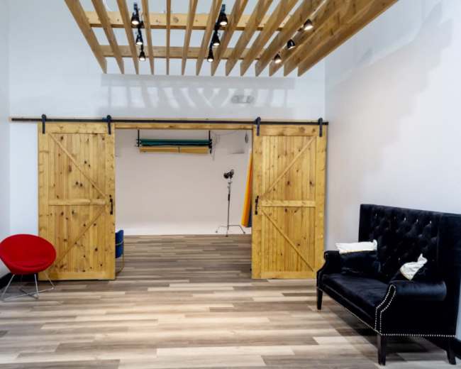 The image shows a spacious interior with wooden sliding doors, a black velvet sofa, and studio lighting equipment in the background.