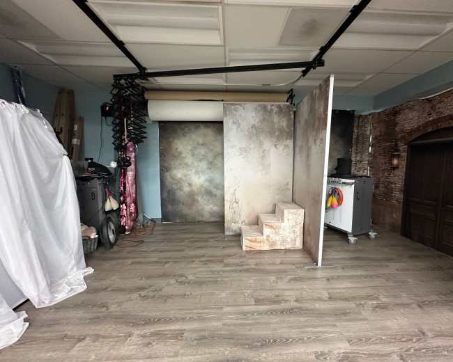 The image shows a photography studio with a wooden floor, backdrops, and a set of stairs leading up to a panel.