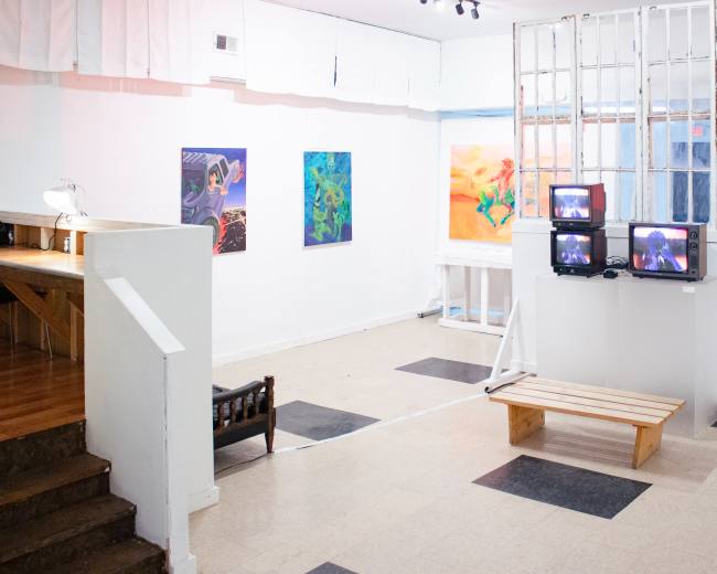 The image shows an art gallery with several colorful paintings on the walls, a wooden bench in the center, and multiple television screens displaying video content.