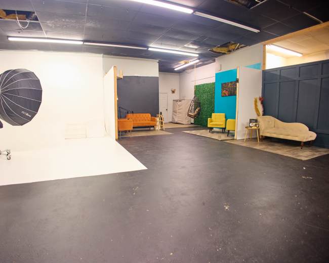 A photography studio with a white backdrop, lighting equipment, and various seating arrangements in different colors.