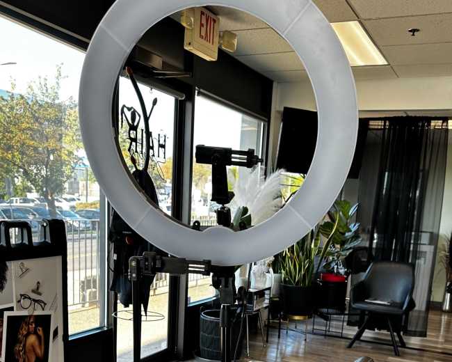 A ring light positioned in front of a black salon chair inside a hair salon.