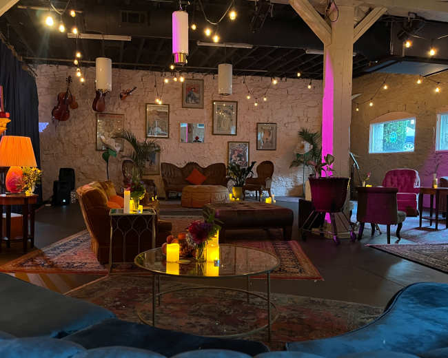 The image shows a cozy lounge area with vintage furniture, soft lighting, and decorative plants, creating an inviting atmosphere.