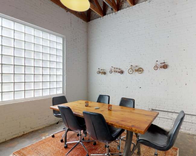 A modern conference room features a wooden table surrounded by black chairs, with bicycle-themed decor on the white brick wall.