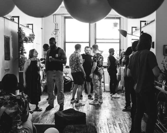A group of people socializes in a well-lit room adorned with balloons and wooden flooring.