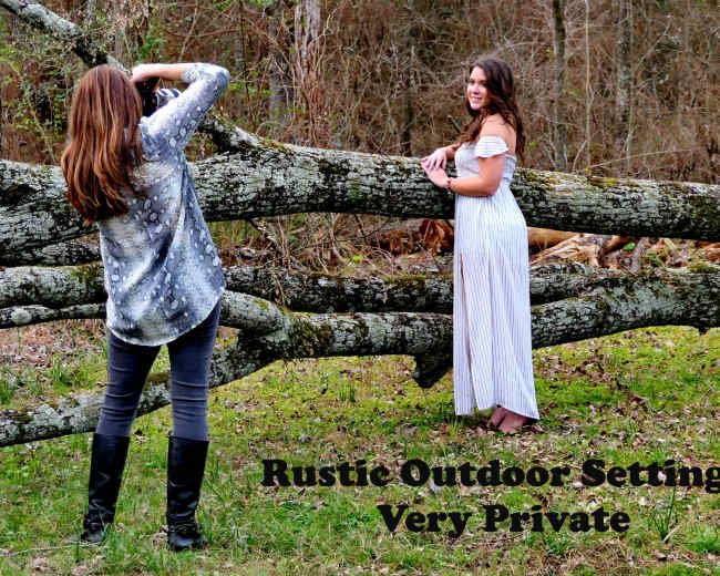 A photographer captures an image of a model posing in a white dress near a fallen log in a wooded area.
