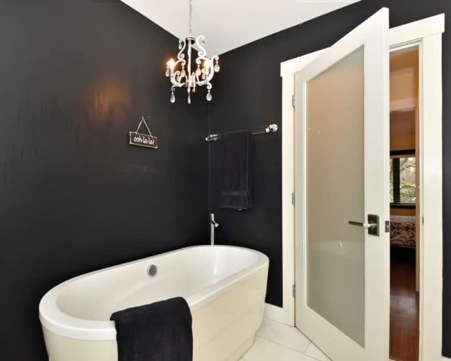 A modern bathroom featuring a freestanding bathtub, a chandelier overhead, and black walls.