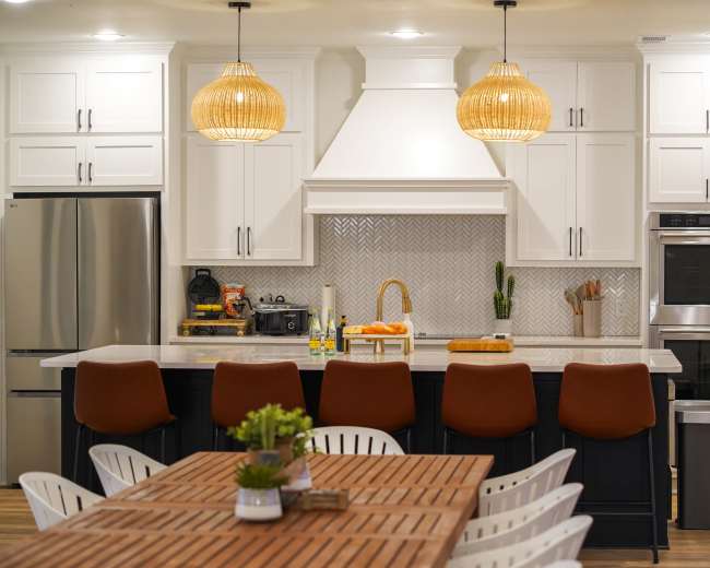The image shows a modern kitchen with white cabinetry, a large island with bar stools, and an adjacent dining table, all featuring a neutral color palette and pendant lighting.