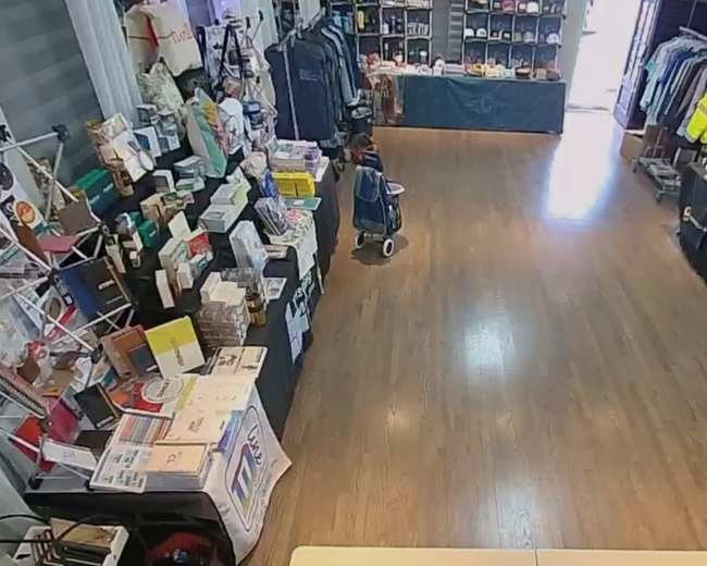 The image shows the interior of a retail store with clothing racks and merchandise displays along the walls and tables.