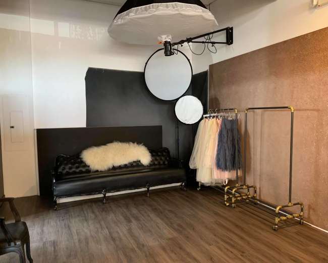 A photo studio featuring a black leather couch, a circular backdrop, and a clothing rack with various pastel-colored garments.