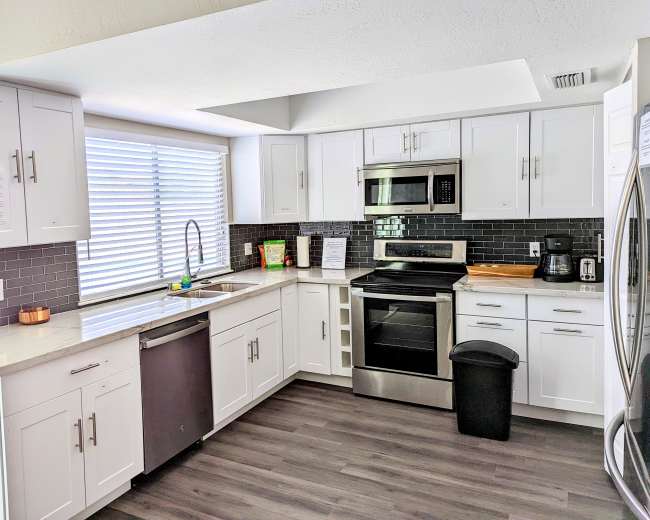 The image shows a modern kitchen featuring white cabinetry, stainless steel appliances, and a gray tiled backsplash.