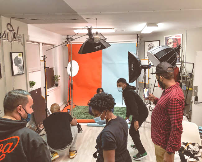 A group of individuals set up a photoshoot in a studio with a colorful backdrop and multiple lighting equipment.