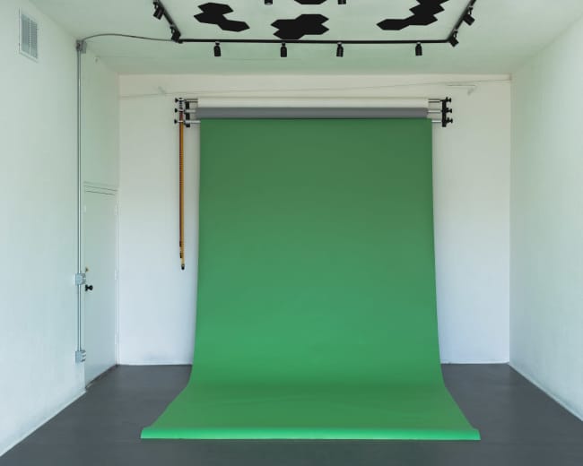 A studio space with a large green backdrop set up against a white wall.