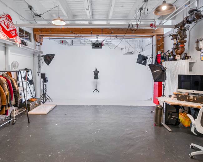 A spacious studio with a white backdrop, a clothing rack with various garments, and professional lighting equipment set up around a mannequin.