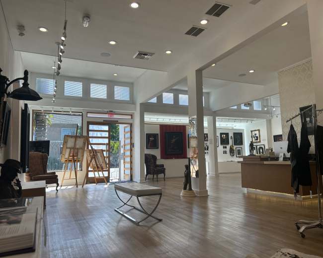 The image shows the interior of an art gallery featuring a spacious layout, art displays on the walls, and an open area with furniture and sculptures.