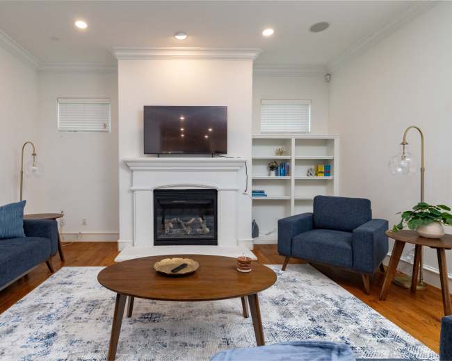 The living room features a fireplace with a television mounted above it, surrounded by blue furniture and a wooden coffee table on a patterned rug.