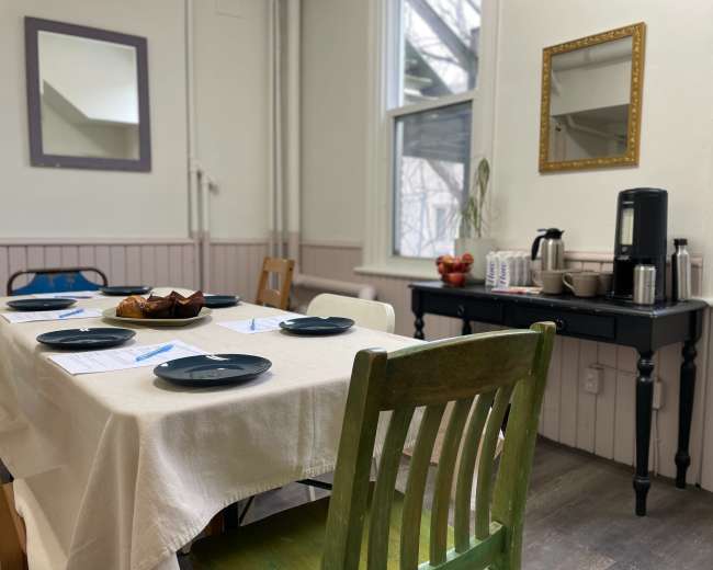 A dining area features a table set with blue plates, a white tablecloth, and a side counter with a coffee maker and snacks.