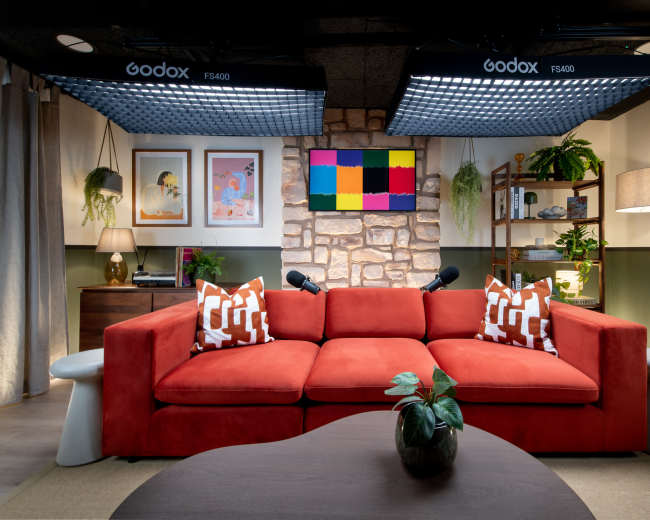 A brightly lit living room features a red sofa with decorative pillows, a coffee table, and a stone accent wall with a colorful screen above it.