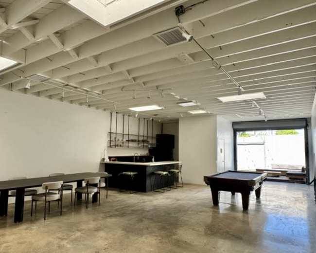 The image shows a spacious interior with a dining table, kitchen area, and a pool table, all under a ceiling with exposed beams.