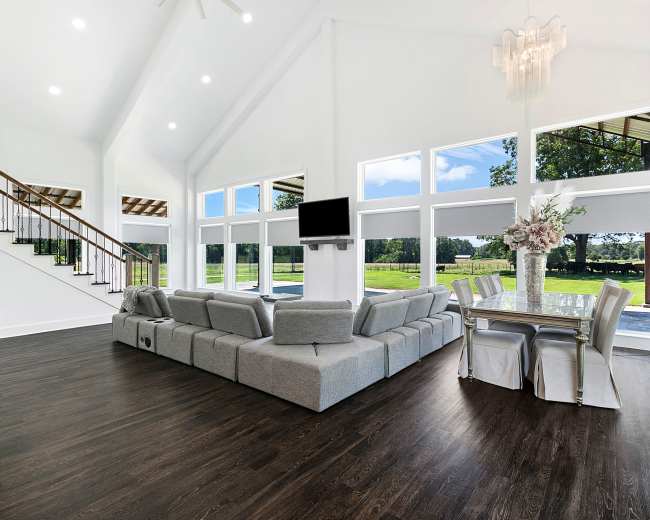 The scene features a spacious, modern living area with large windows, a sectional sofa, a dining table, and elegant decor.