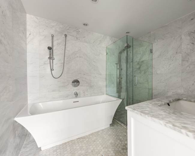 The bathroom features a white freestanding tub, a glass shower enclosure, and marble walls with a mosaic tile floor.
