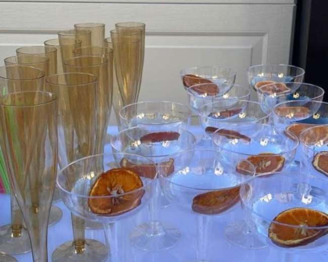 The image shows an assortment of clear and golden champagne glasses arranged on a table, each garnished with a slice of dried orange.