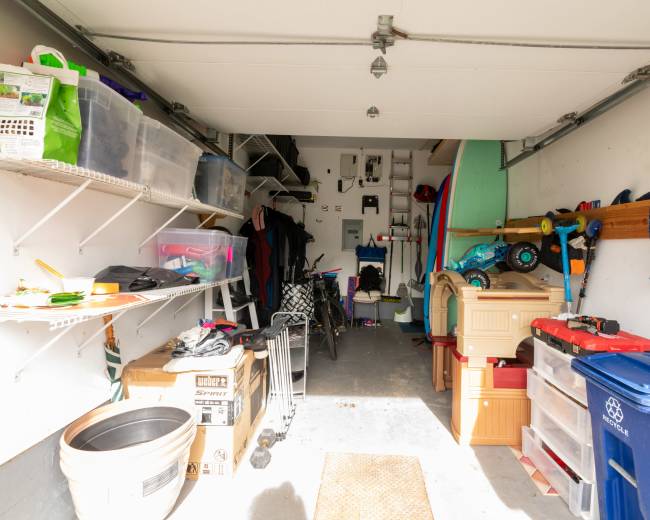 The image shows a cluttered garage with various storage bins, tools, and sporting equipment organized along the walls and floor.