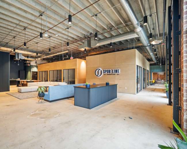 The image shows a spacious office interior featuring modern design elements, including a reception area, meeting rooms with glass partitions, and industrial-style lighting.