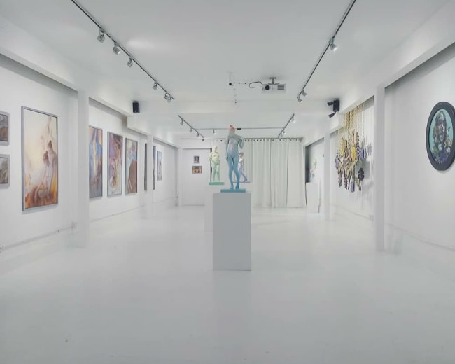 An art gallery with white walls displaying various paintings and sculptures, including a central figure on a pedestal.