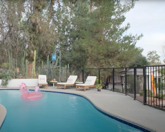 A swimming pool features a blue water slide, a pink flamingo float, and three lounge chairs beside it.